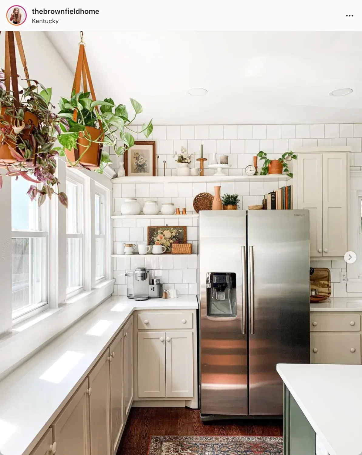 A kitchen with cream Accessible Beige cabinets, white subway tile and plants hung at the window