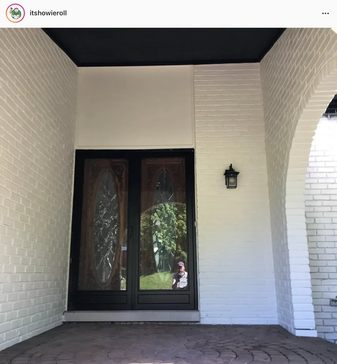 A white-painted brick entry porch with black double doors and a lantern