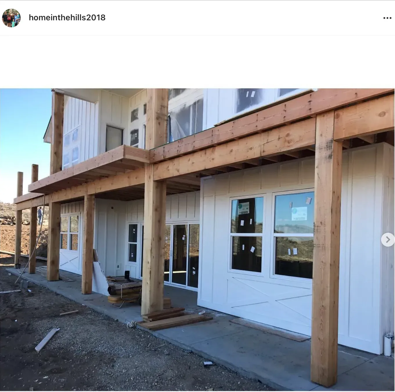A house exterior in white board-and-batten siding with a raw timber porch, still being built