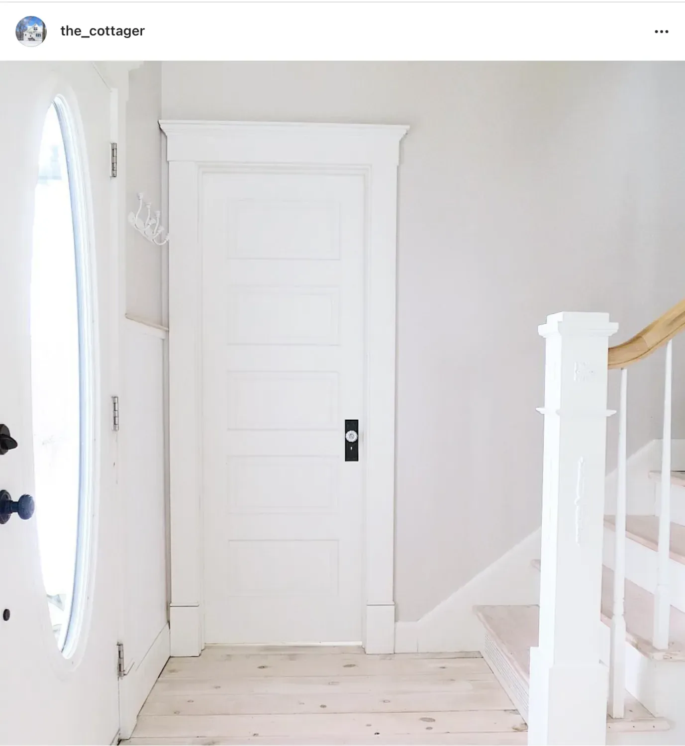 A white entry with a five-panel door, an oval glass front door and pale pine floors