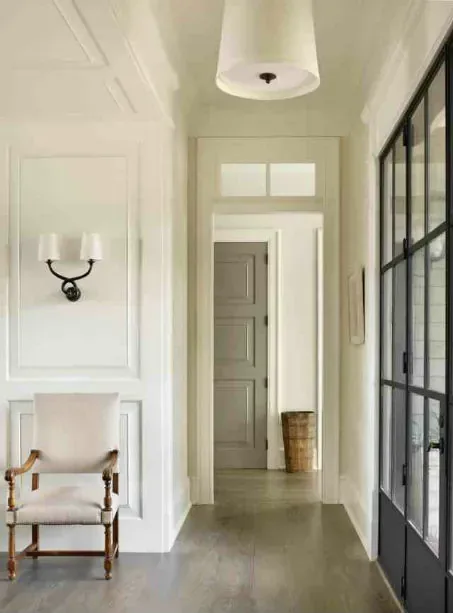 A panelled hallway lit by a large drum flush mount and a black double-arm sconce