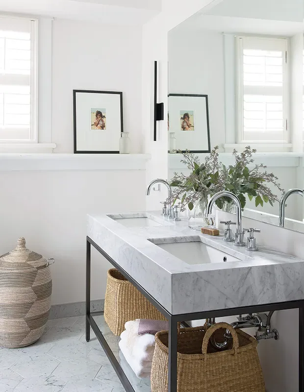 A marble double vanity on a black metal frame with a slim black vertical sconce at the mirror