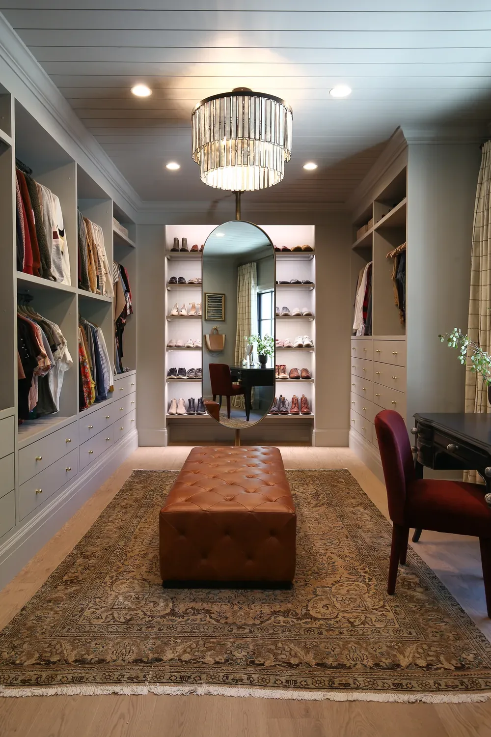 A walk-in closet of built-in wardrobes and drawers around a tufted leather ottoman