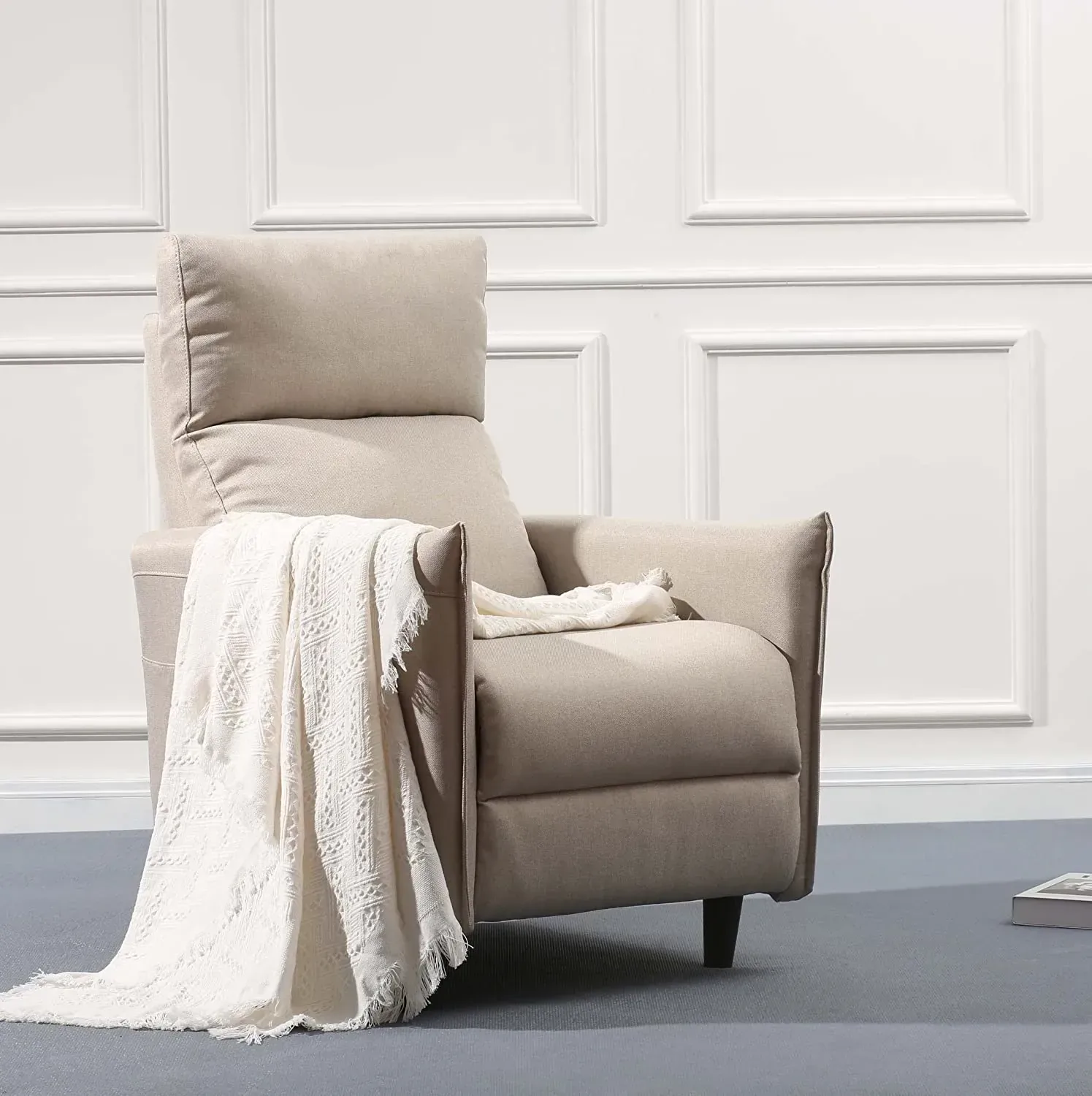 A beige upholstered recliner with slim wood-edged arms, a fringed throw over one side