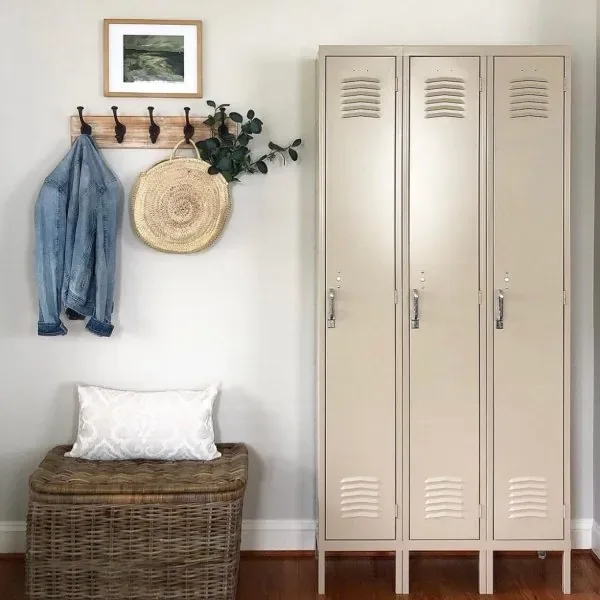 A mudroom with three tall greige lockers beside a coat rail and a wicker trunk