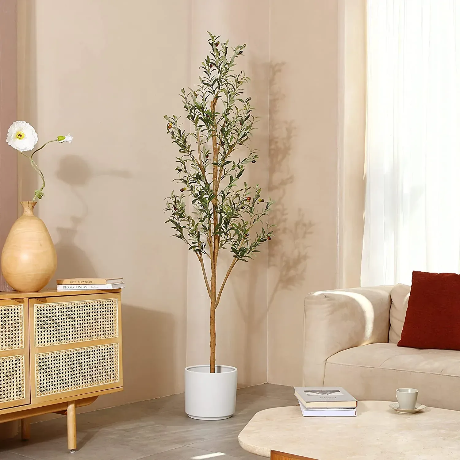 A faux olive tree hung with olives in a white pot beside a rattan sideboard
