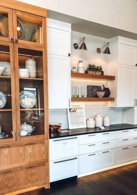 Warm under-shelf lighting glowing beneath open wood shelves in a white and oak kitchen
