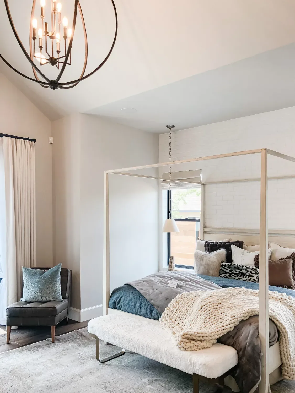 A bedroom with a canopy bed under a black orb chandelier, a chunky knit throw across the foot