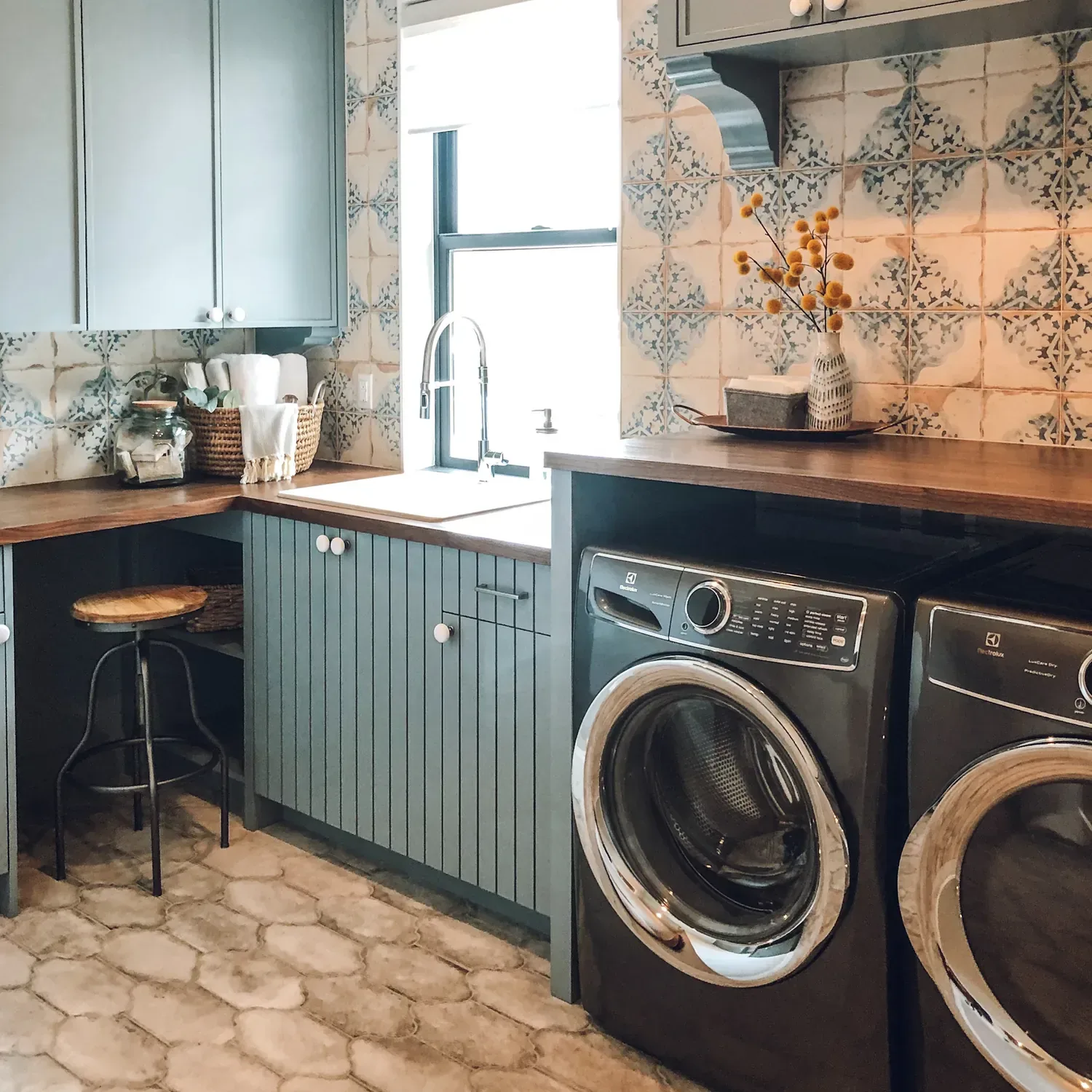 A laundry room with sage-green built-in cabinets, patterned tile backsplash and a walnut counter