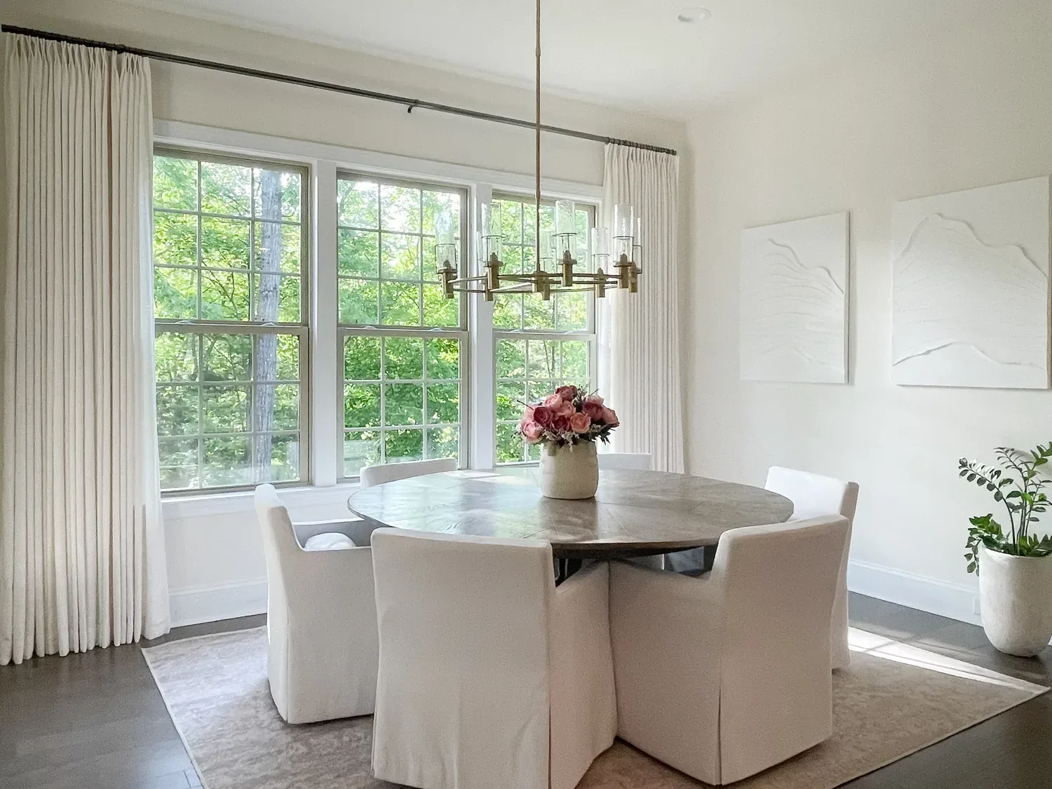Ivory pinch pleat drapes at the dining room windows, a round table and slipcovered chairs