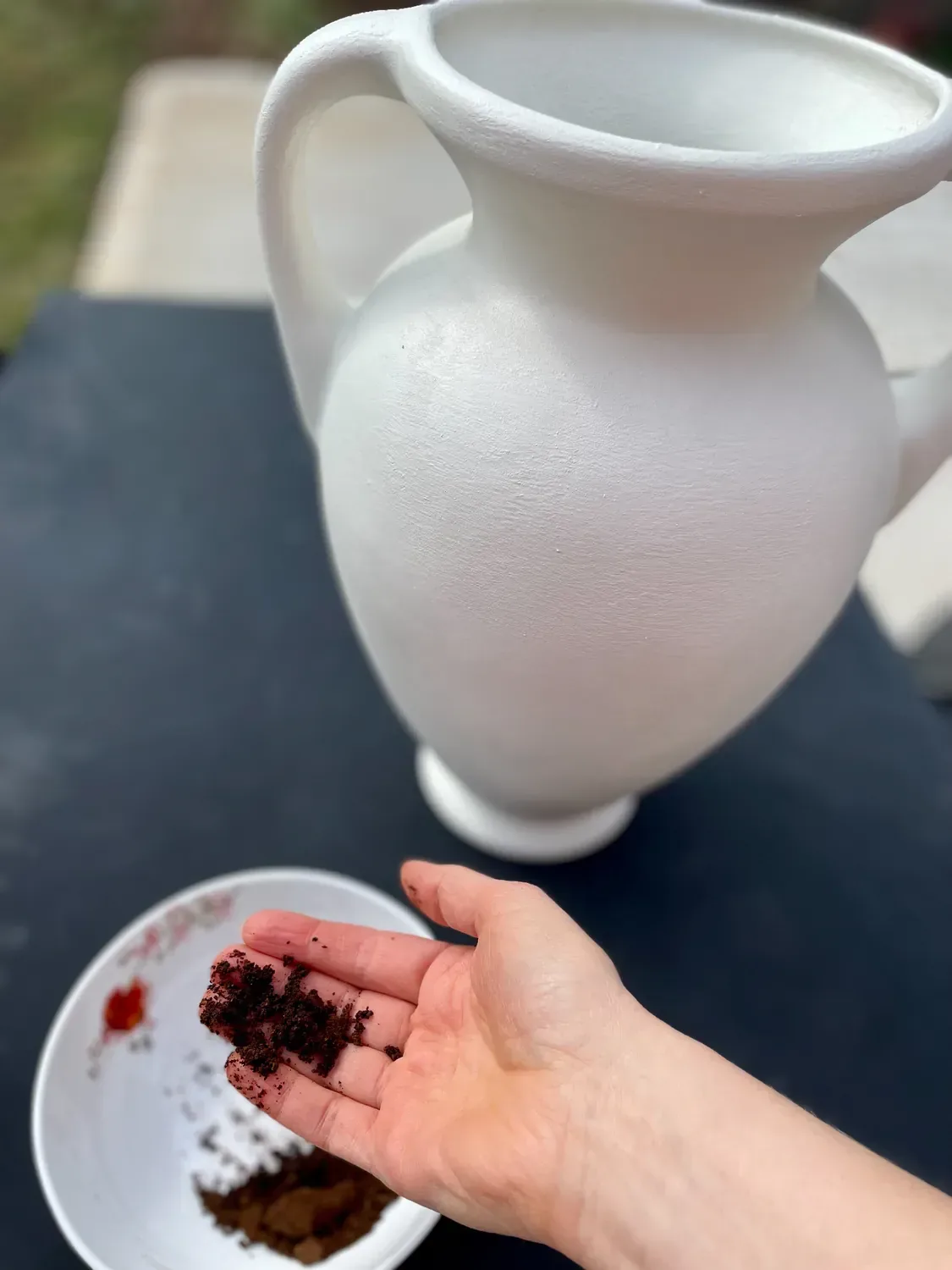 A handful of damp coffee grounds held beside the finished vase, ready to be rubbed on