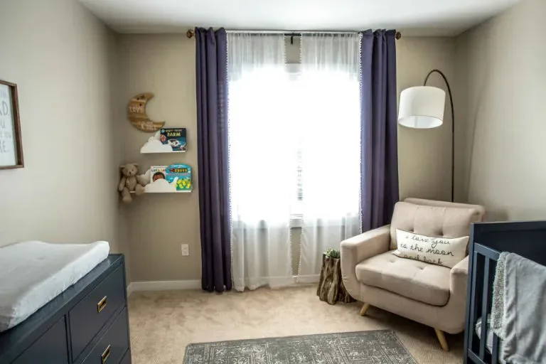 A nursery corner with navy curtains, a cream armchair and picture-book ledges beside the window