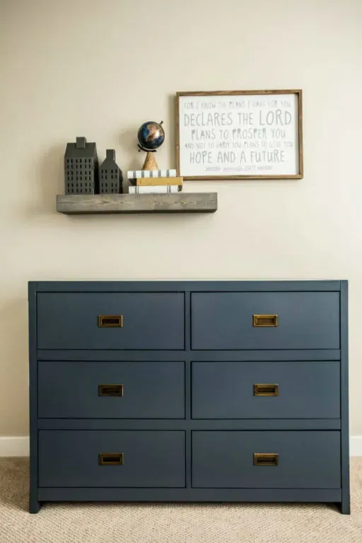 A shelf of skyline blocks, a globe and a framed scripture above the navy campaign dresser