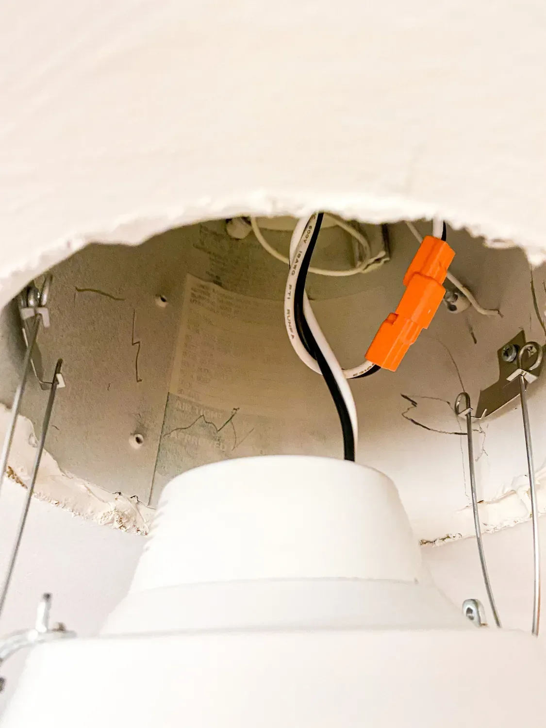 The new LED light held in the ceiling opening by two spring clips, wiring and connector above