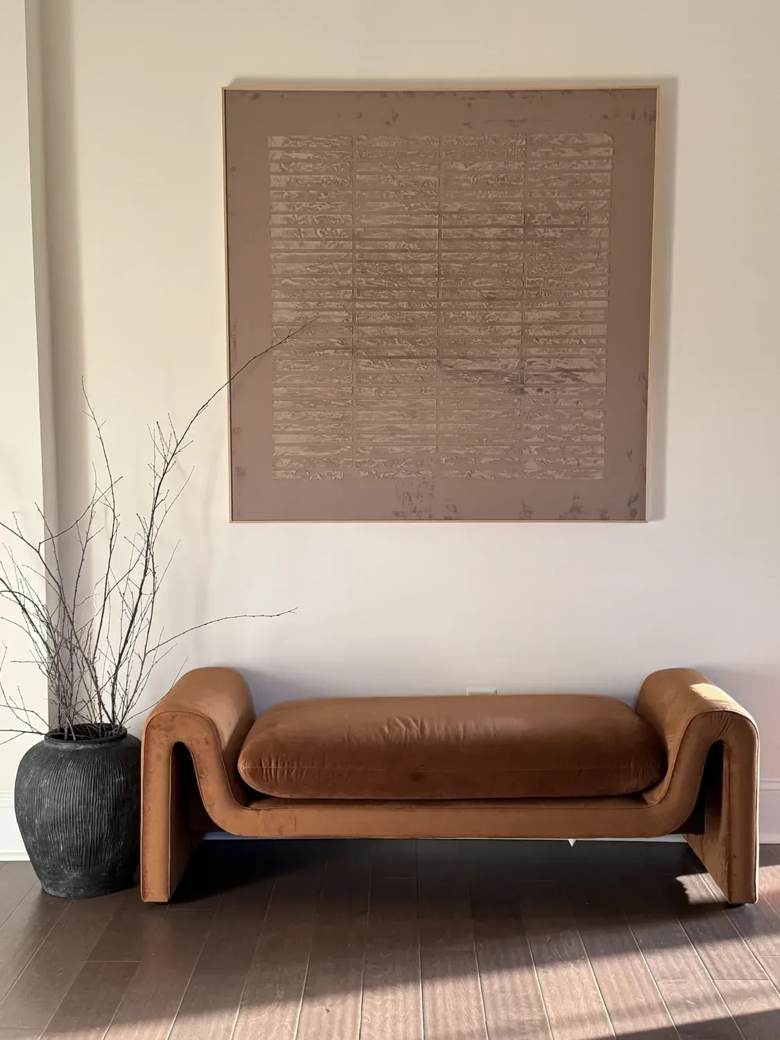 The finished hallway: a large textured canvas above a tan leather bench and a vase of branches