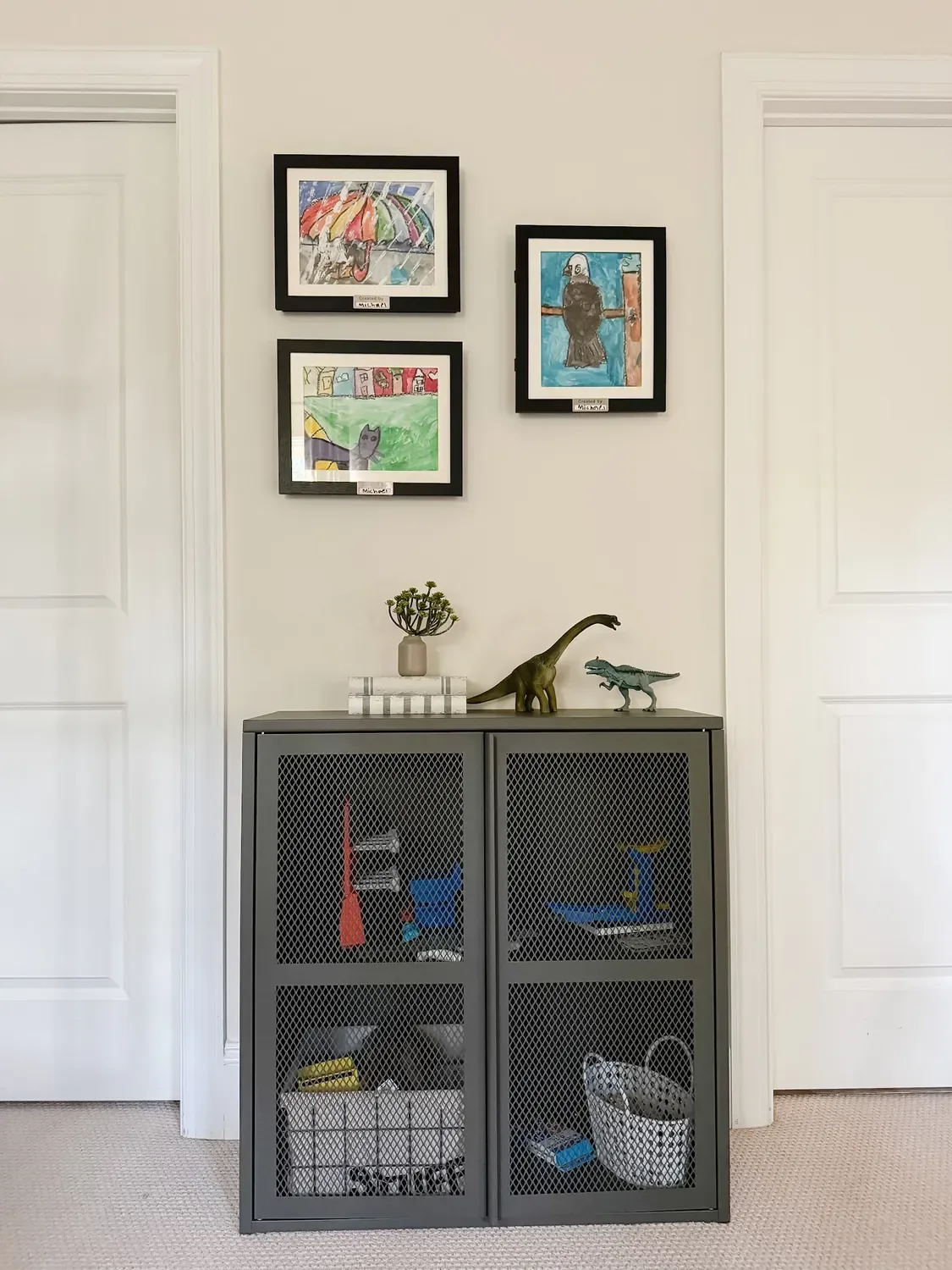 The framed gallery wall between two doors, the mesh cabinet of toys beneath it