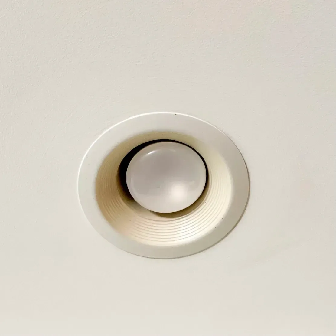 A recessed can light with a yellowing trim ring and an old halogen bulb