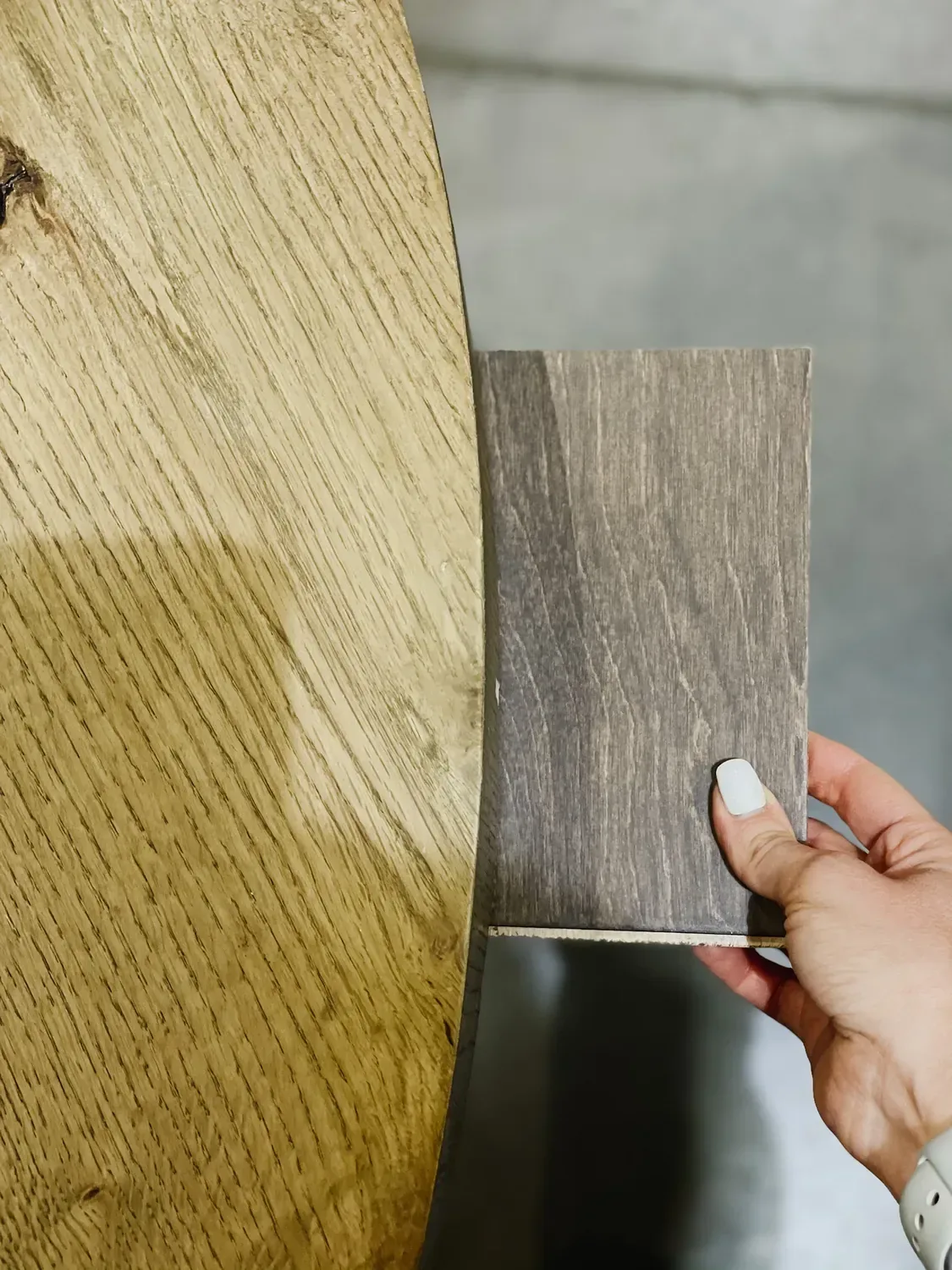 A grey-toned wood sample held against a light raw oak table