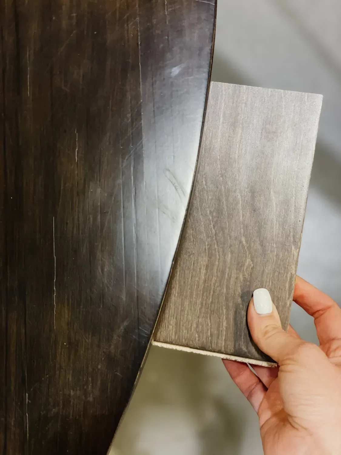 A wood floor sample held against a dark stained table top to compare the tones