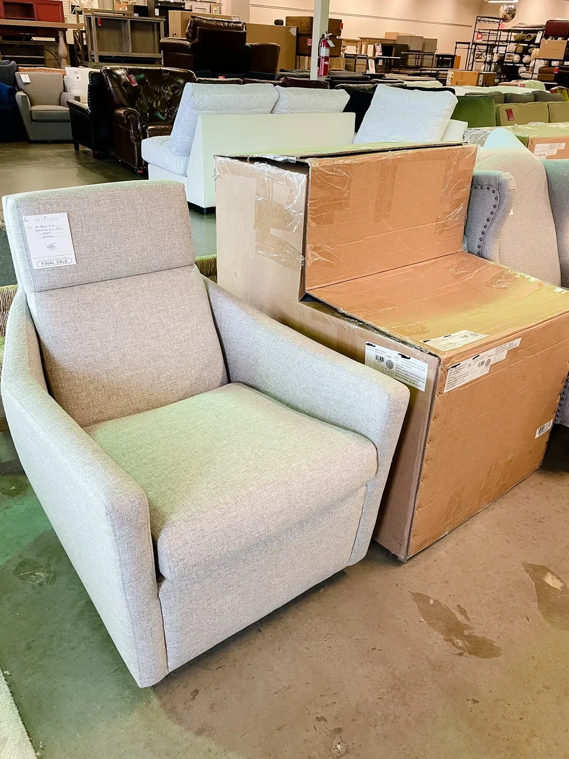 A grey armchair on the outlet floor beside the boxed, unopened version of the same chair