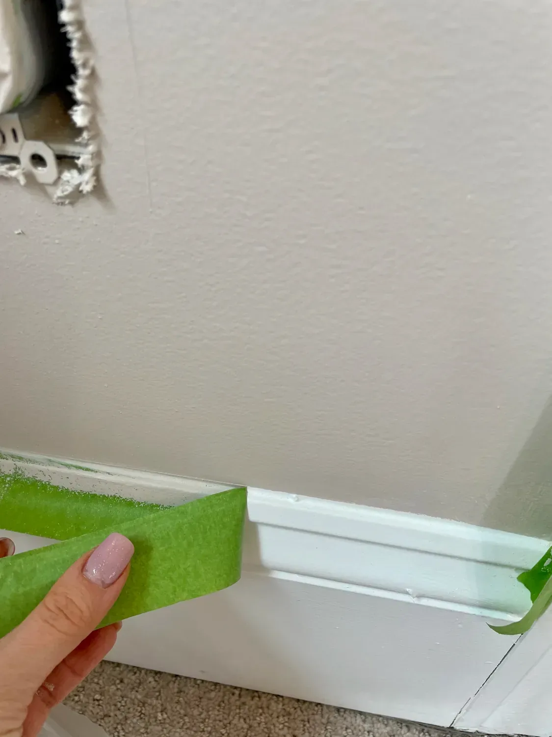 Green painter's tape pressed along the top edge of the baseboard before painting