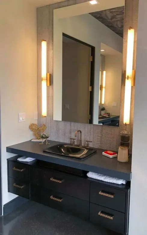 A floating dark vanity with tall vertical bar lights flanking a grasscloth-framed mirror
