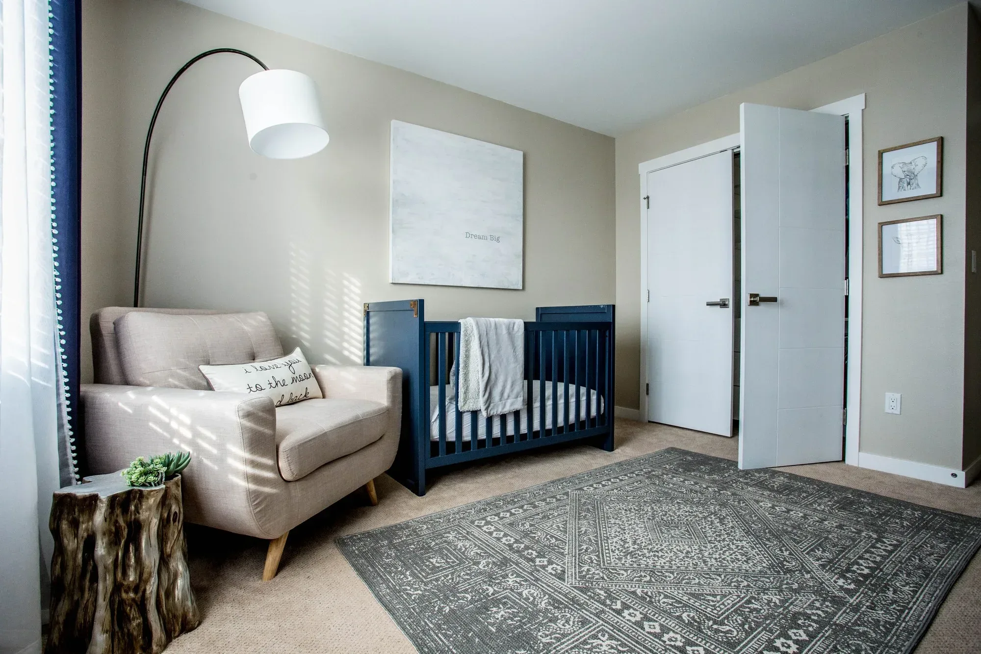 Nursery with a navy crib, an arc lamp and a linen chair by the window