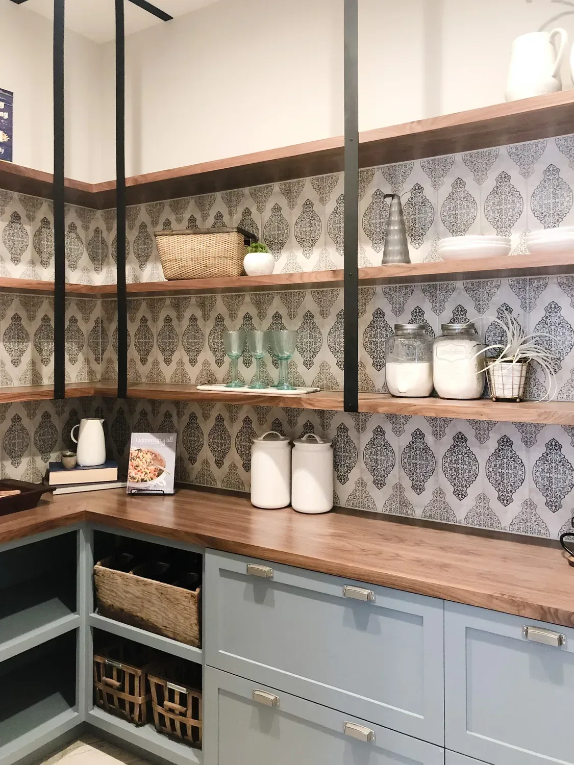 A pantry with open walnut shelves on black brackets over blue-grey cabinets