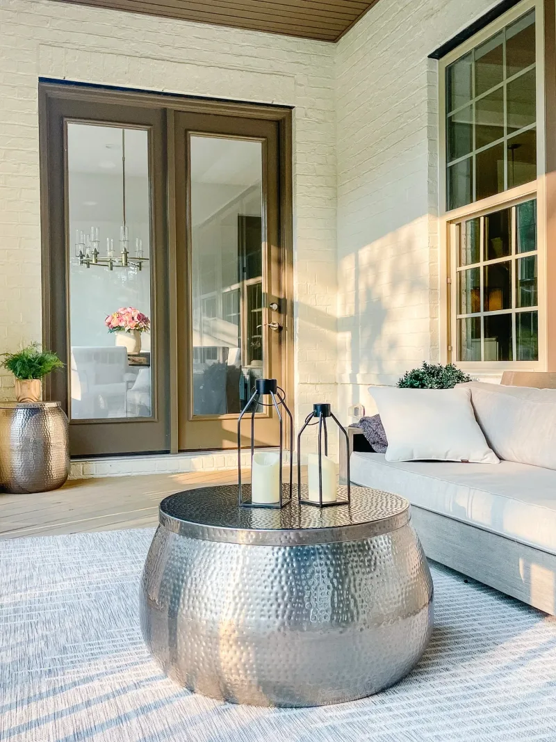 Covered porch with a hammered silver drum table, lanterns and a cream sofa