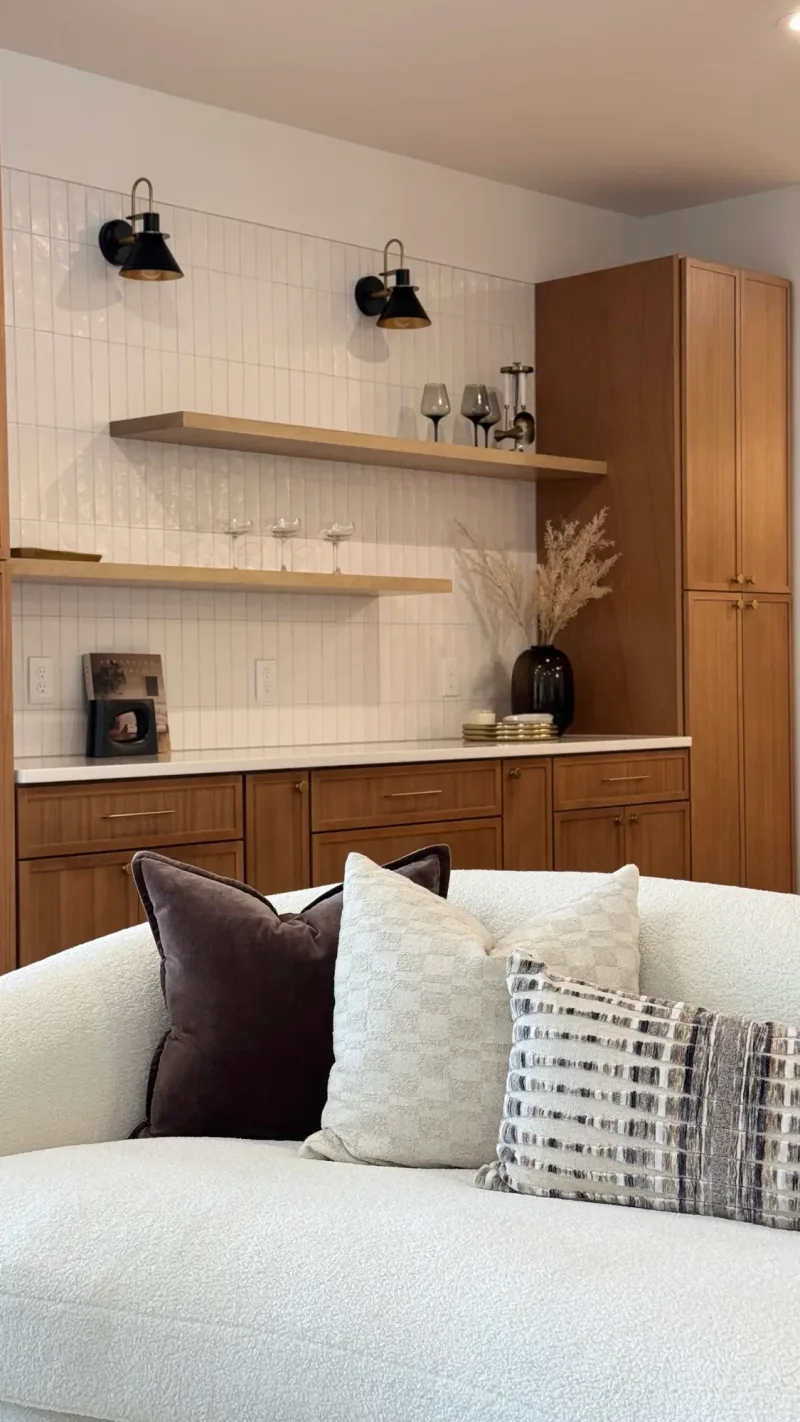 Built-in bar with walnut cabinets, floating shelves and black sconces