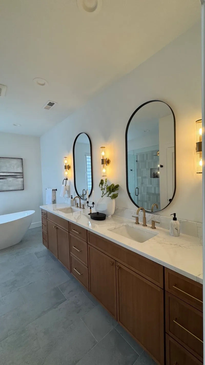 The full bathroom, with a double vanity, oval mirrors and the tub beyond