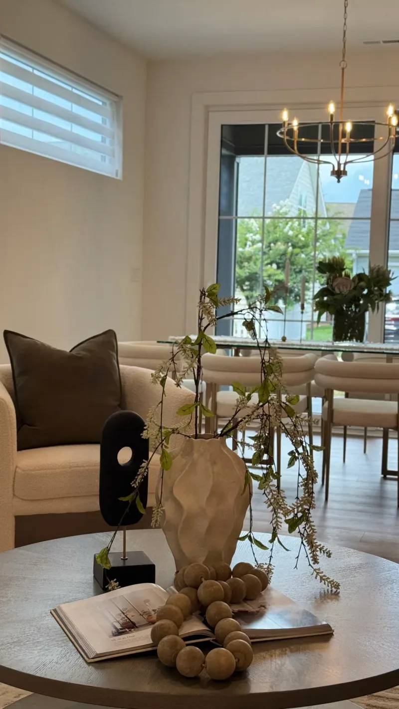 Round coffee table styled with a stone vase and trailing greenery, the dining table beyond