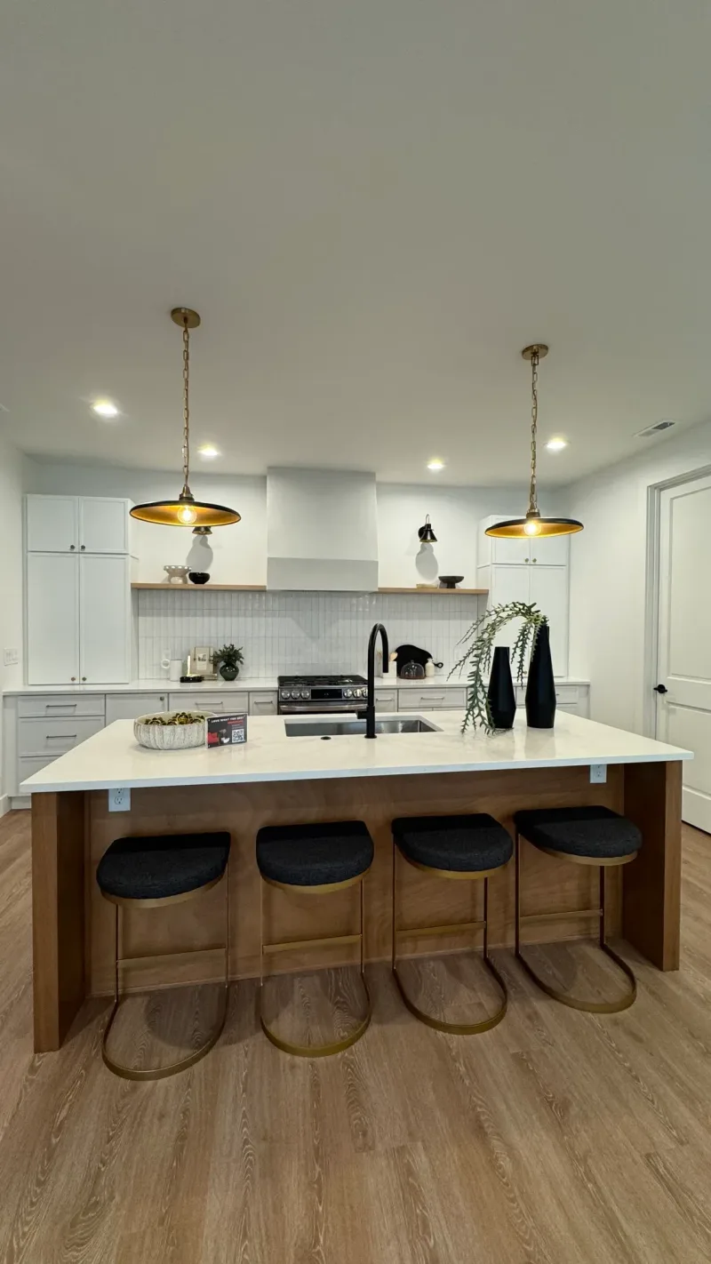 White kitchen with a walnut island, brass pendants and four black stools