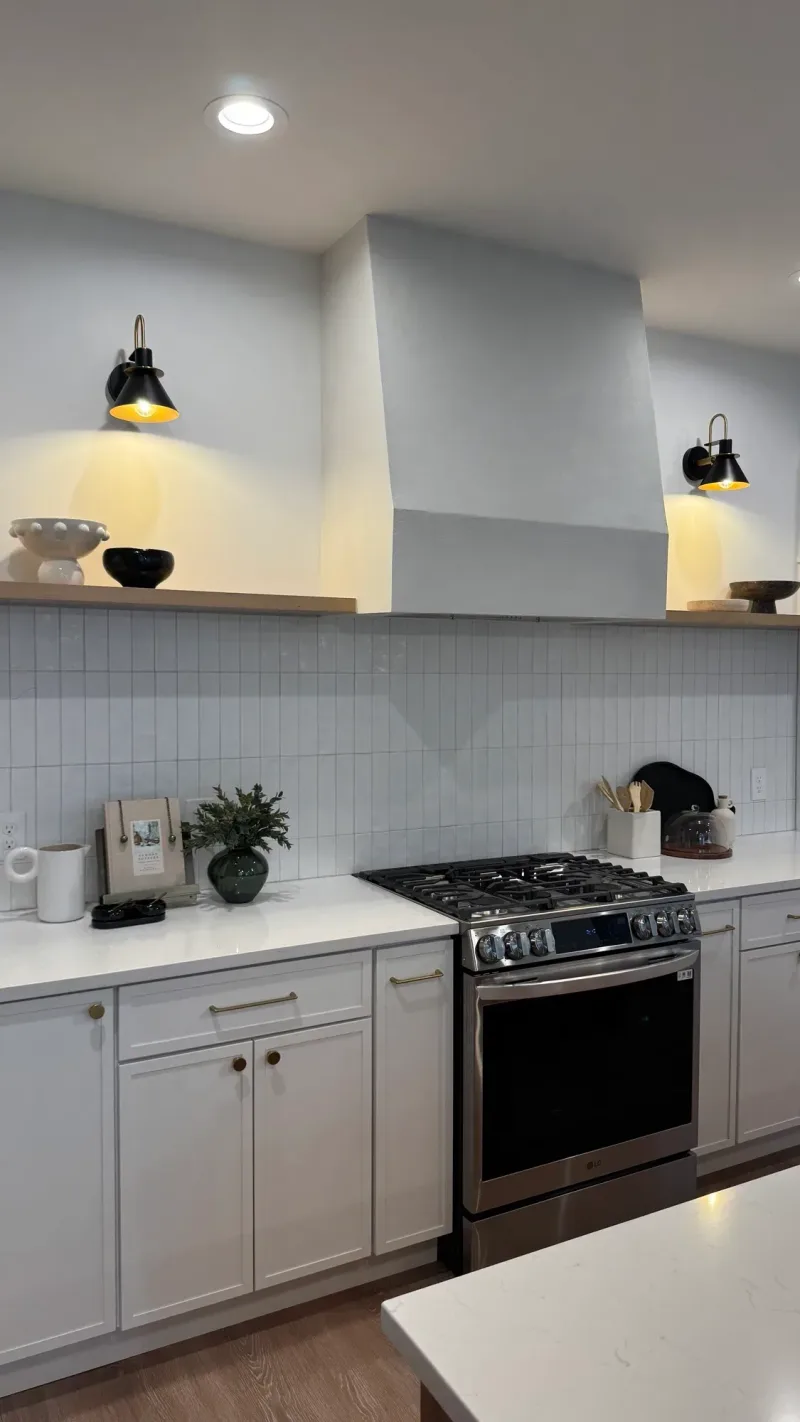 Range wall with a plaster hood, open shelving and a pair of black sconces