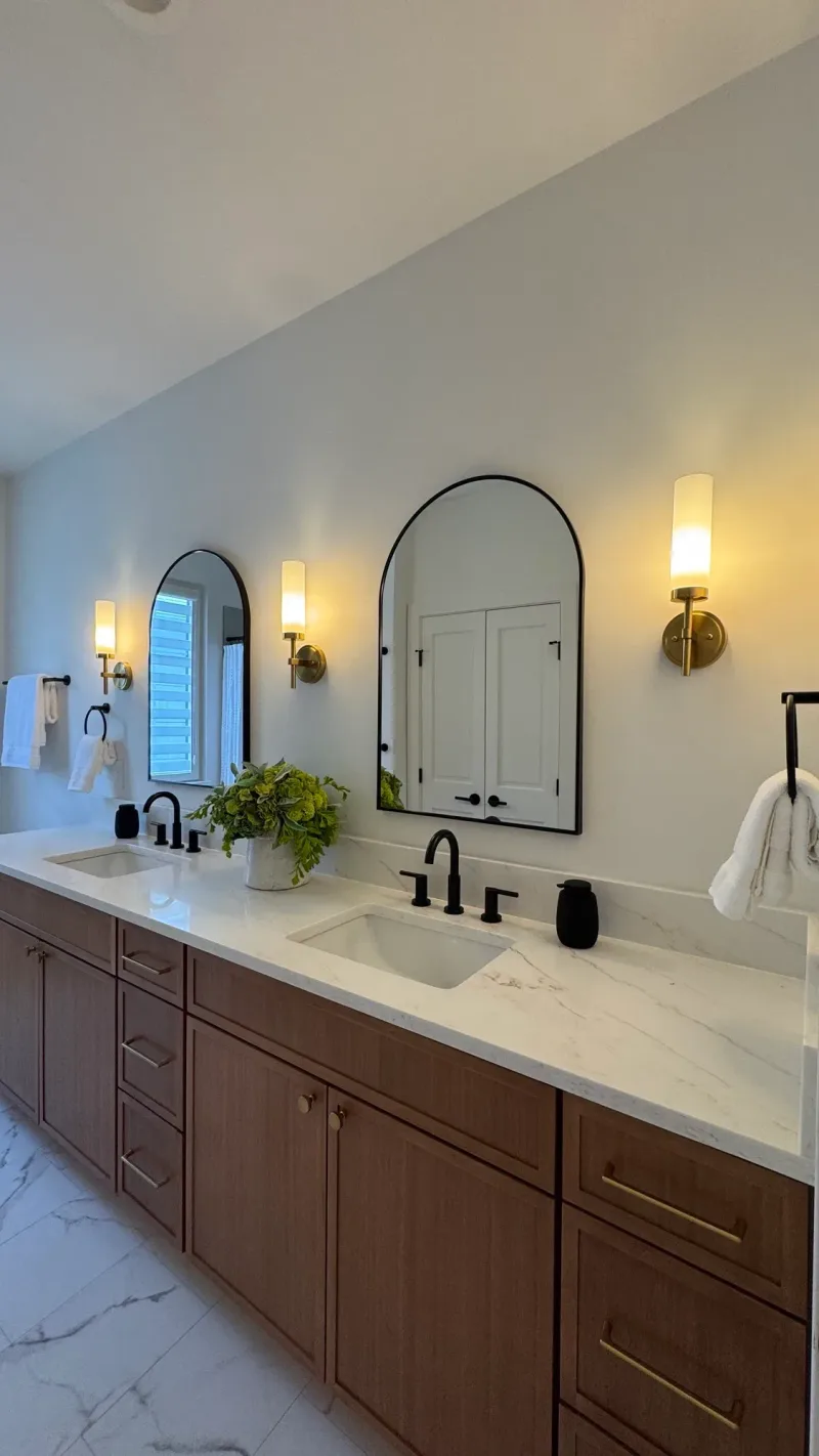 Double vanity in walnut with a marble counter and an arched black mirror