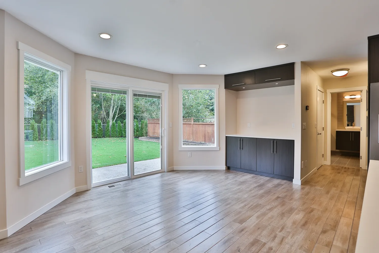 Dining area with sliding glass doors onto a lawn, dark built-in sideboard and upper cabinets, pale wood floor