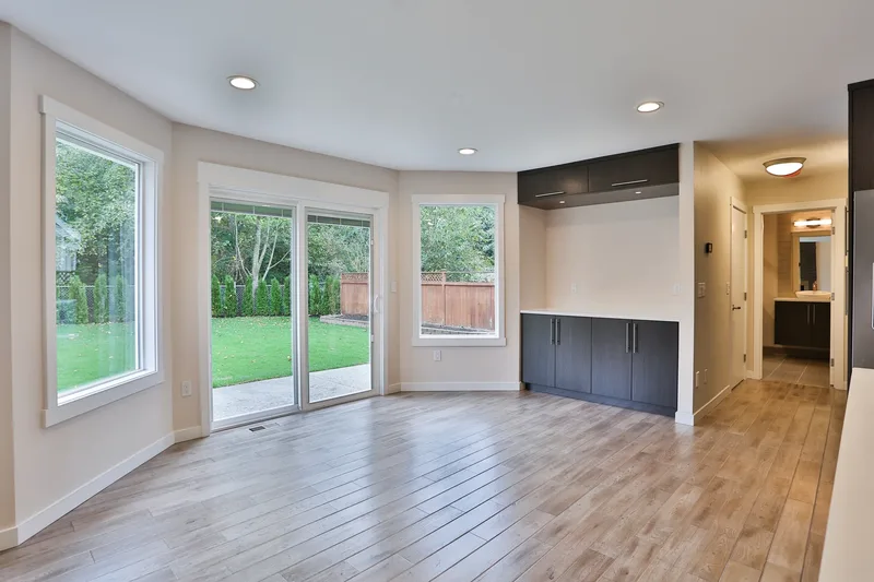 Dining area with sliding glass doors onto a lawn, dark built-in sideboard and upper cabinets, pale wood floor
