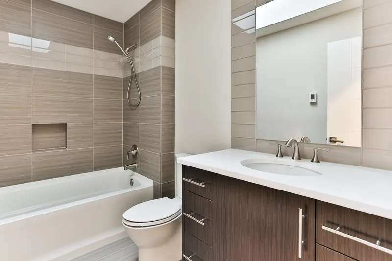Hall bathroom with an alcove tub, tiled surround and recessed niche, white counter on dark vanity cabinetry