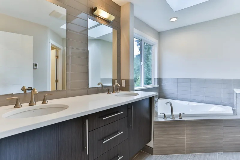 Primary bathroom double vanity with two undermount sinks and a mirrored wall, corner jetted tub under the window