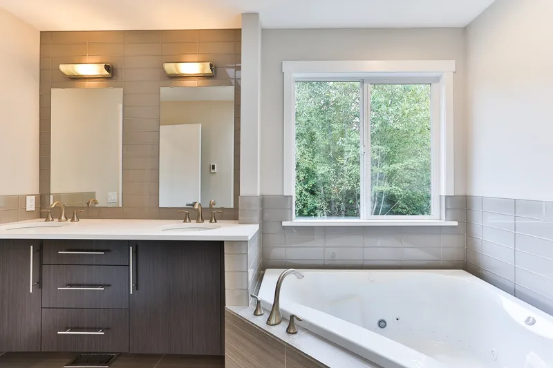 The primary bath from the tub side, twin mirrors and sconces above the dark double vanity