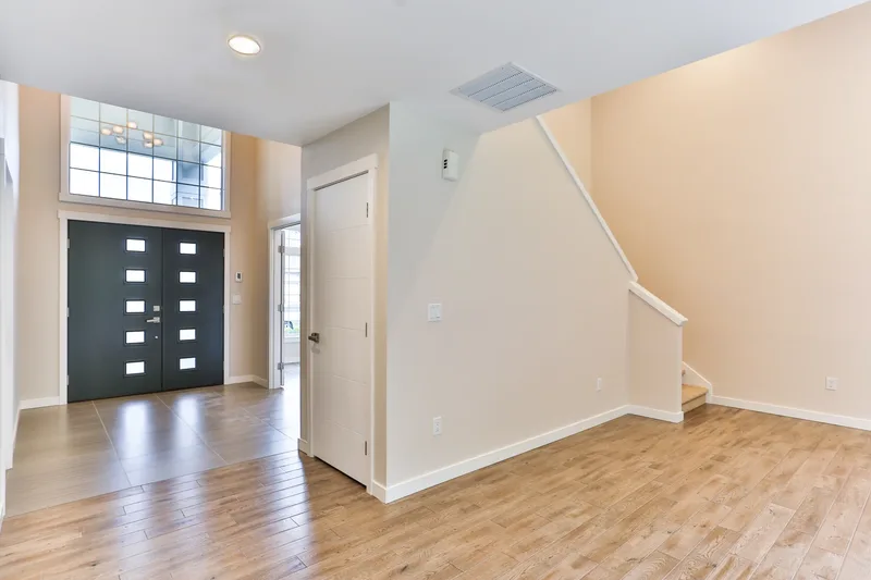 Entry hall from inside, black double front door with glazed panels, transom window above, staircase at right