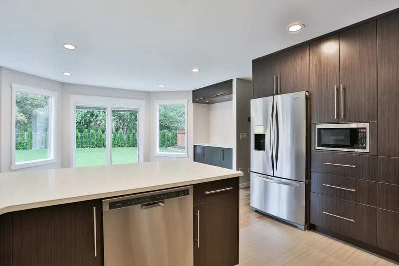 Quartz peninsula with a stainless dishwasher, tall dark pantry cabinets and built-in microwave, windows onto the garden