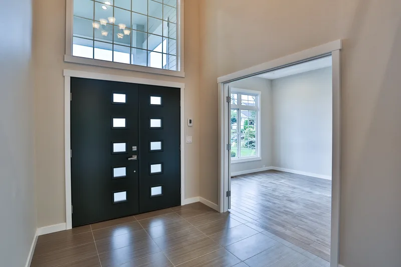 The front doors from inside the foyer, frosted glass panes, gridded transom above, tile meeting wood