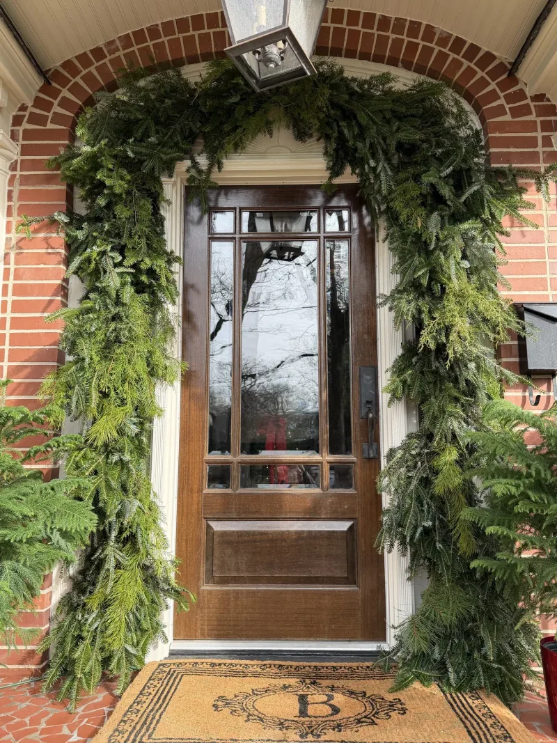 Front door framed by a cedar garland arch, with a monogrammed doormat