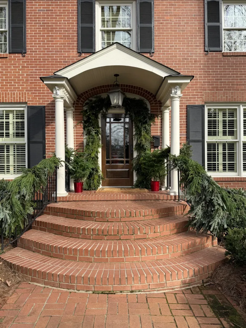 Brick colonial porch dressed with garland and candles down the front steps