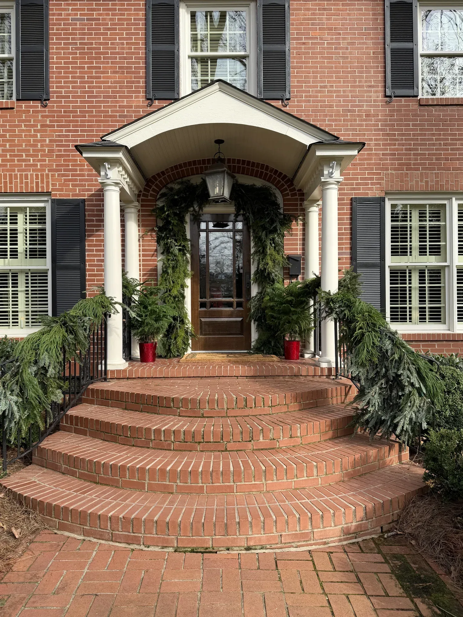 Brick colonial porch dressed with garland and candles down the front steps