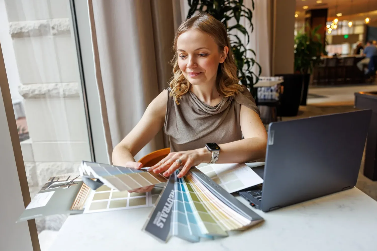 Tatyana at a table with Sherwin-Williams fan decks spread open beside a laptop