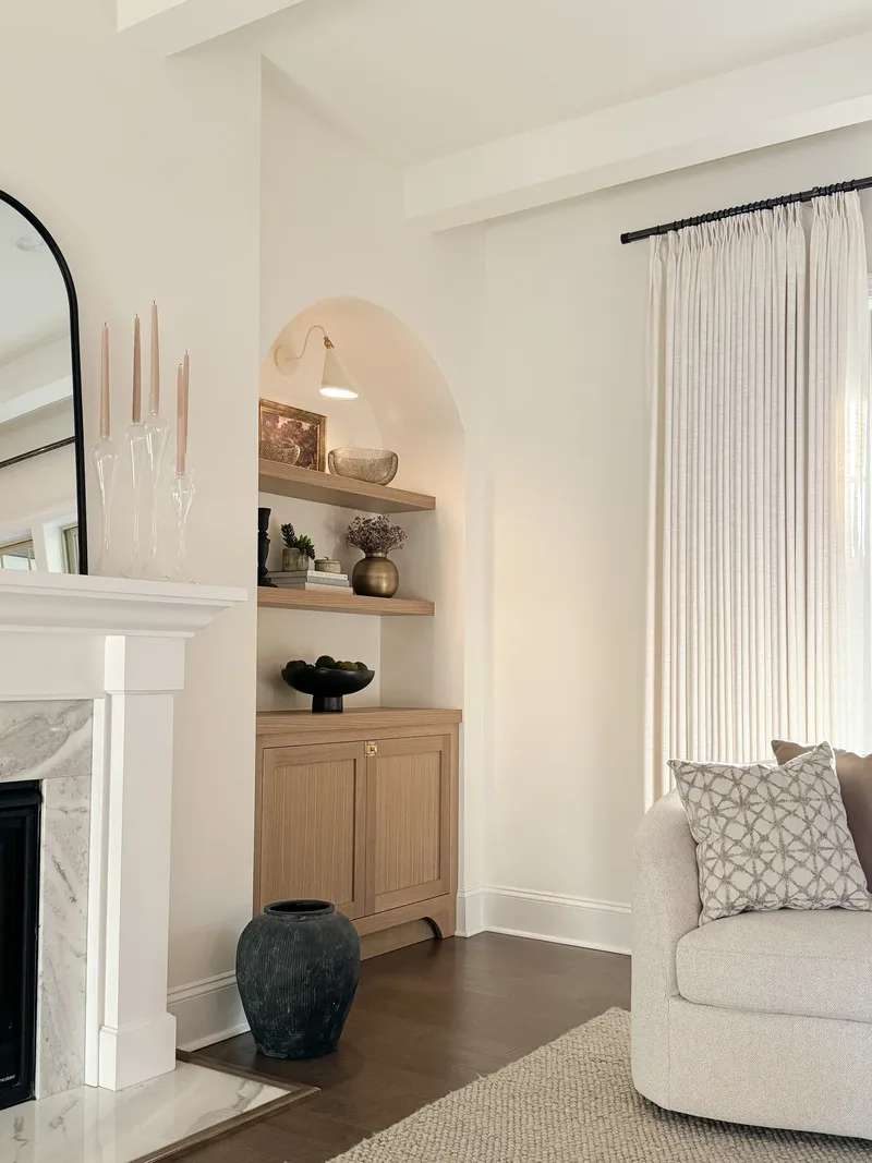 White marble mantel at left beside an arched oak built-in, black urn on dark wood floor
