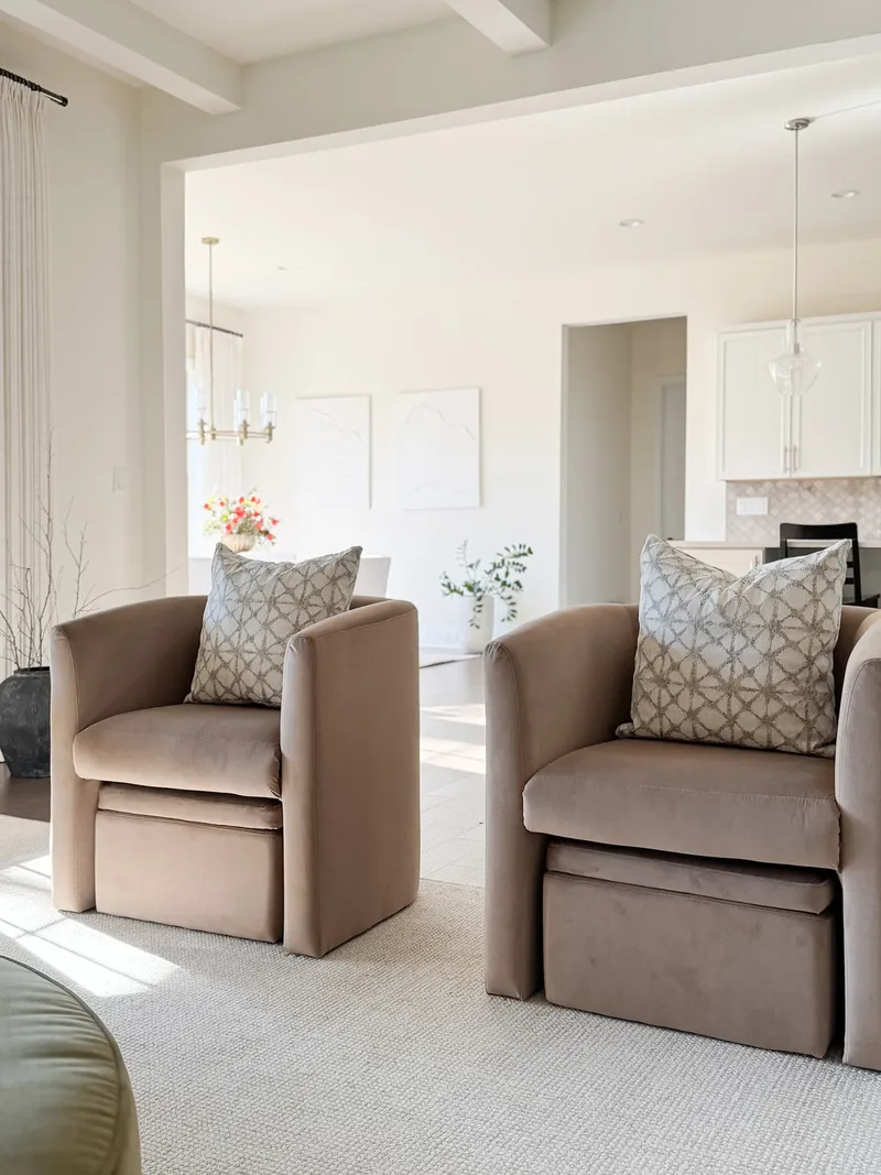 Caramel velvet armchairs in the foreground, the dining room and kitchen visible through the opening beyond