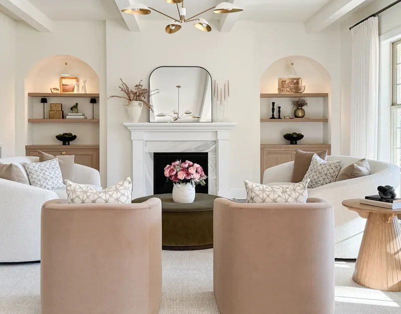 The fireplace wall stepped in closer, roses on the olive ottoman between two blush velvet chairs